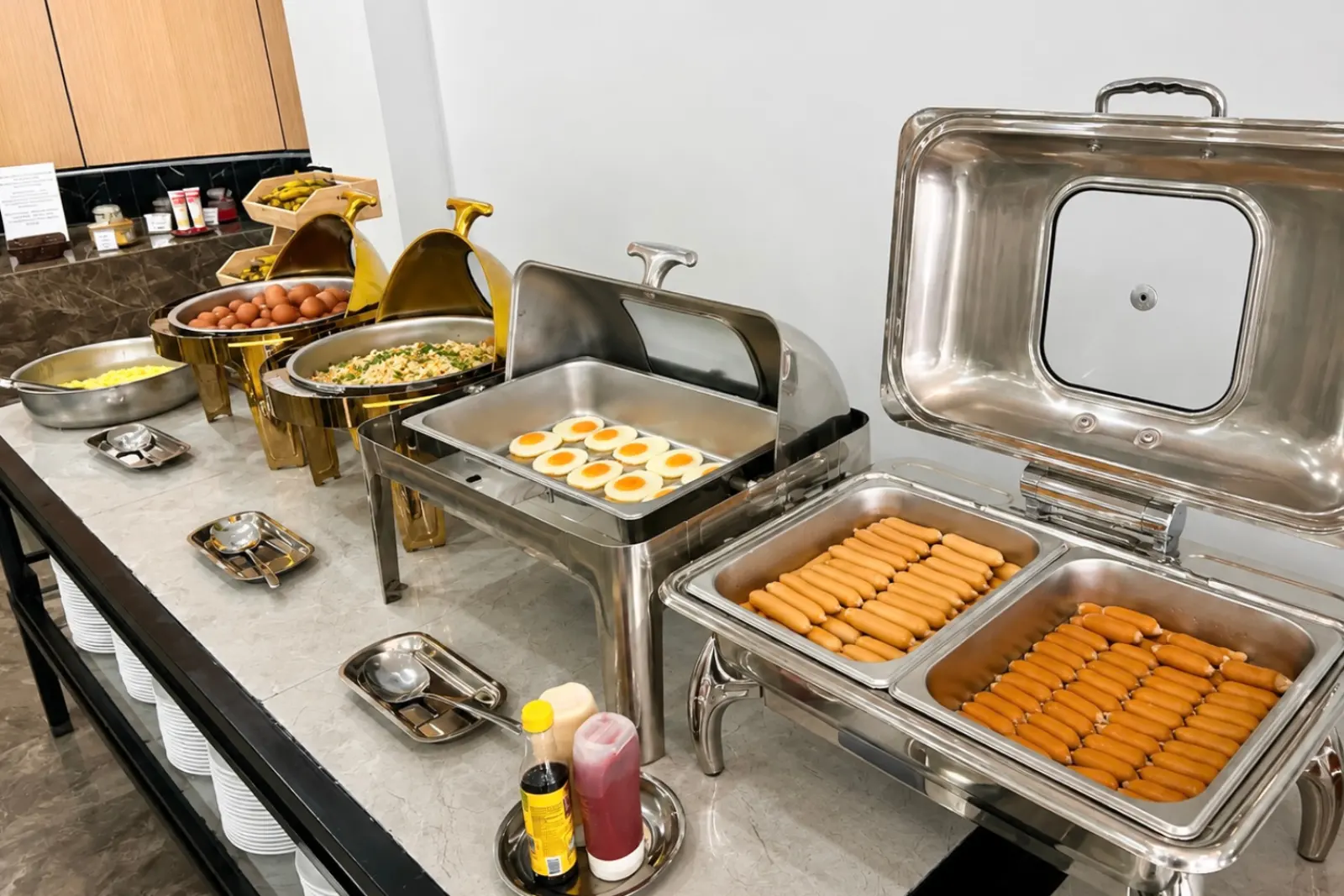 Breakfast buffet line with gold chafing dishes, eggs, sausages and fresh herbs