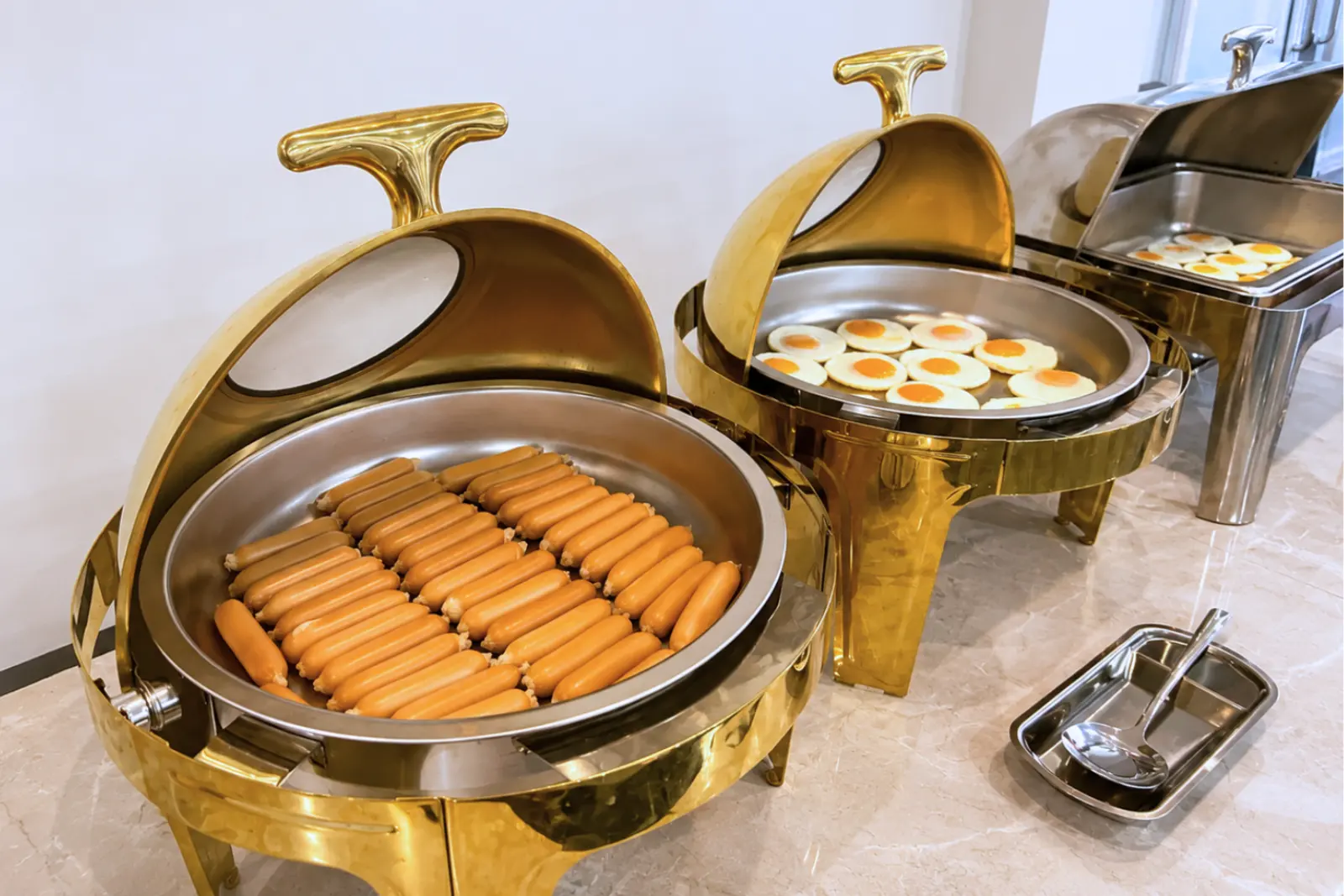 Sausages and fried eggs in gold chafing dishes on the buffet